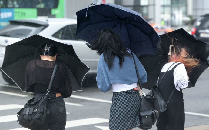 서울·인천·경기 지역에 호우주의보가 내려진 23일 오후 서울 여의도에서 시민들이 강풍을 견디고 있다. 연합