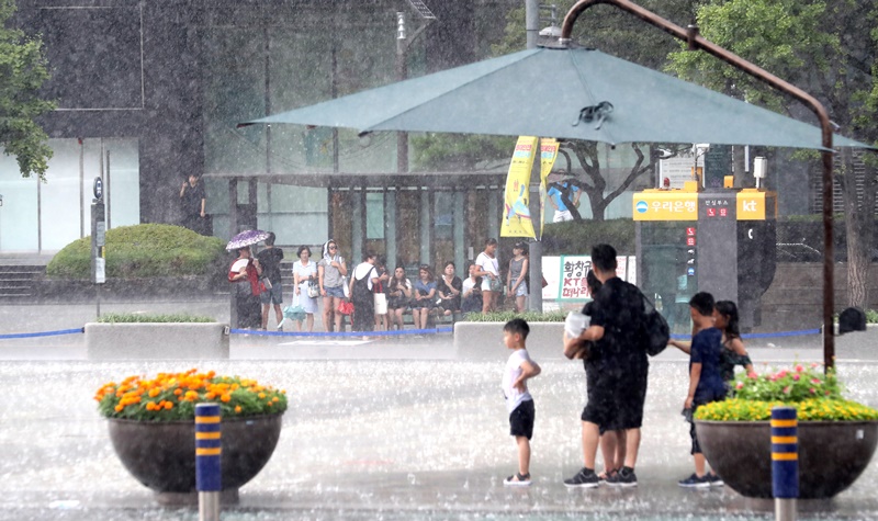 ▲ 폭염이 계속된 28일 서울 광화문 광장에 한때 강한 소나기가 내리자 시민들이 주변 시설물에서 비를 피하고 있다. 연합